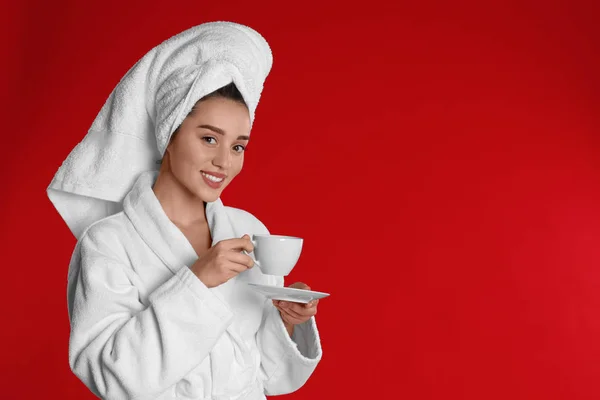 Kırmızı arka planda bir fincan kahveyle bornozlu genç bir kadın. Sp — Stok fotoğraf