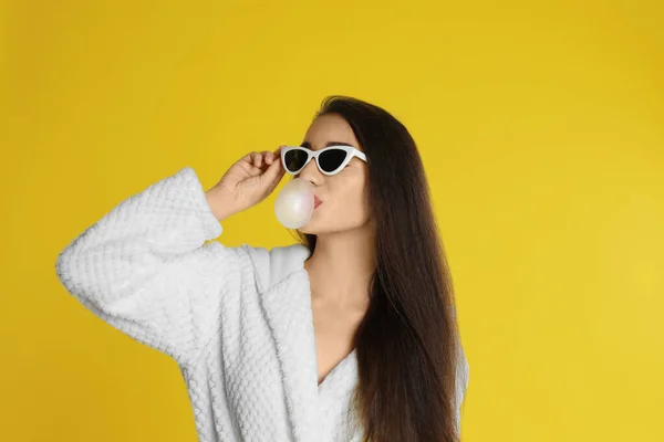 Mladá žena v županu a slunečních brýlích foukání žvýkačky na vás — Stock fotografie