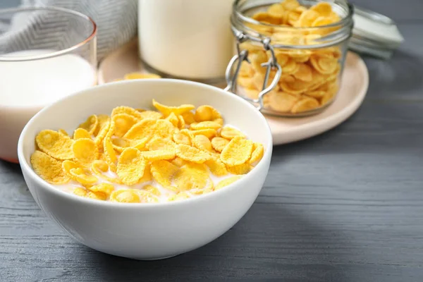 Tasty crispy corn flakes with milk on grey wooden table