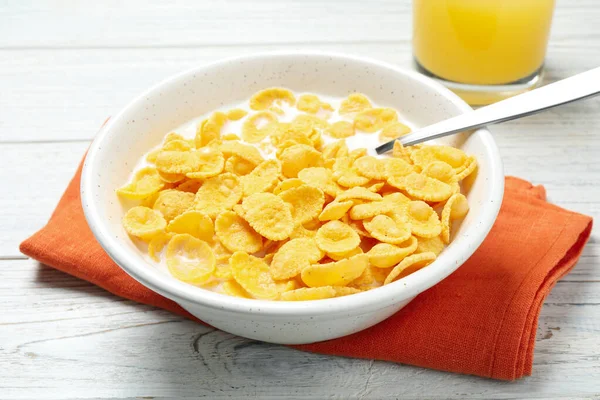 Tasty corn flakes with milk on white wooden table