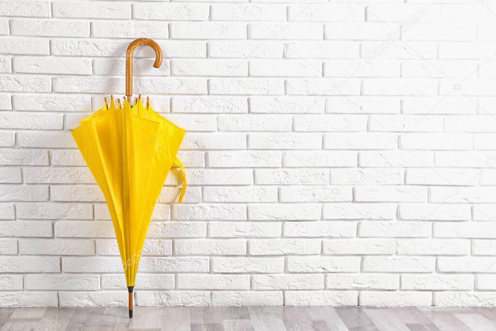 Beautiful yellow umbrella near white brick wall. Space for text