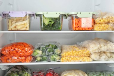 Buzdolabında farklı donmuş sebzeler olan plastik torbalar ve kaplar.