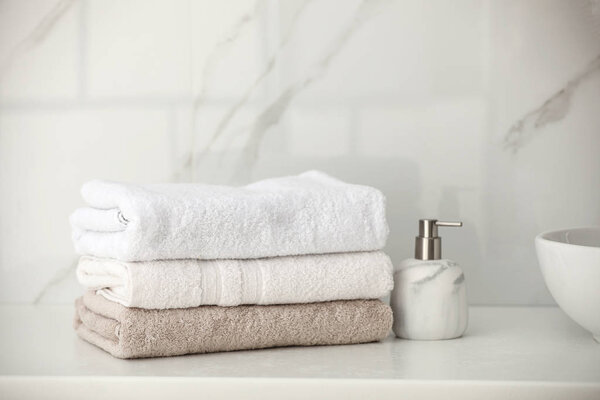 Stack of fresh towels and soap dispenser on countertop in bathroom