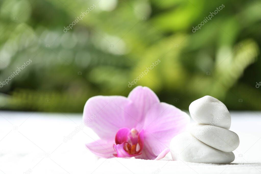 Stack of white stones and beautiful flower on sand against blurred green background. Zen, meditation, harmony