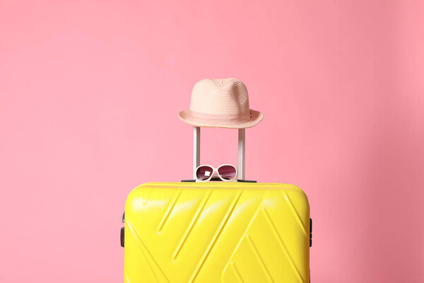 Yellow suitcase with sunglasses and hat on pink background