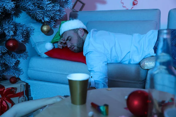 新しい年のパーティーの後にソファの上で寝てサンタの帽子をかぶって酔って男 — ストック写真