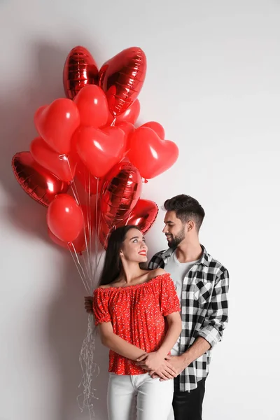 Feliz pareja joven con globos en forma de corazón en el fondo de la luz — Foto de Stock