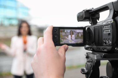 Şehir caddesinde çalışan genç erkek gazeteci ve video operatörü, kamera ekranına odaklanın