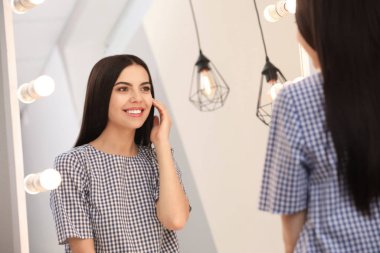 Genç ve çekici bir kadın evinde kendine şık bir aynada bakıyor.