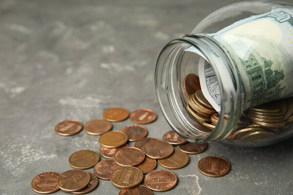 Overturned glass jar with money on grey stone table, closeup