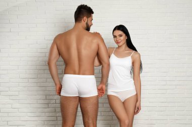 Duvarın yanında beyaz iç çamaşırlı genç bir çift.