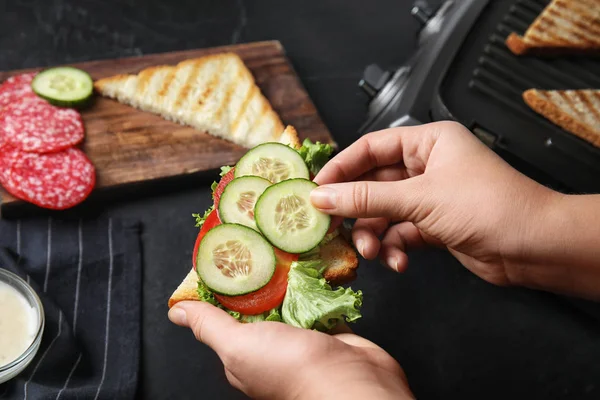 Woman adding cucumber to sandwich at black table, closeup