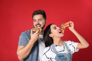 Kırmızı arka planda pizza yiyen duygusal genç çift.