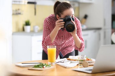 Yemek blogcusu öğle yemeğini içeride ahşap masada çekiyor.
