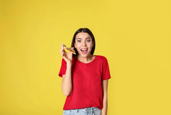 Эмоциональная женщина с вкусной пиццей на желтом фоне — стоковое фото
