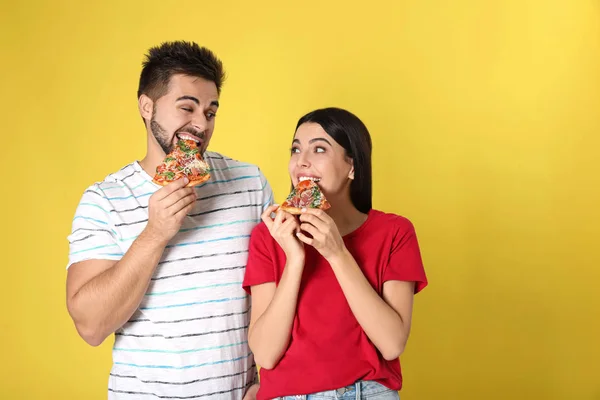 Emotional couple eating pizza on yellow background