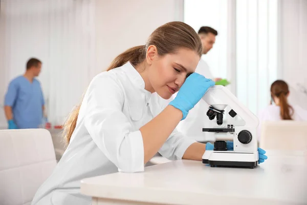 Científico usando microscopio en la mesa y colegas en el laboratorio — Foto de Stock