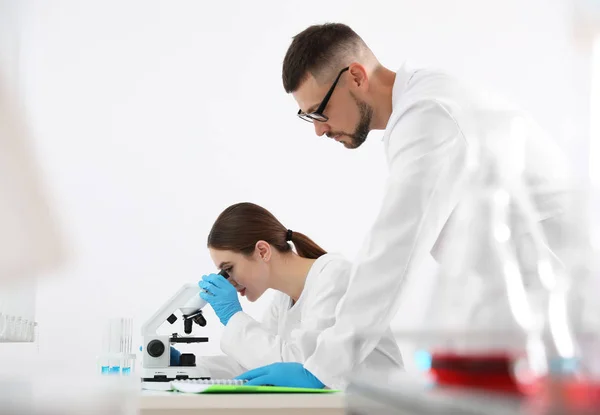 Científico usando microscopio en la mesa y colega en el laboratorio . —  Fotos de Stock