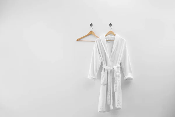 Soft comfortable bathrobe hanging on white wall, space for text — Stock Photo, Image