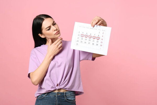 Плотная молодая женщина с календарем с отмеченными днями менструального цикла на розовом фоне

