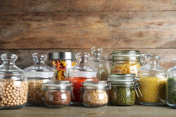 Glass jars with different types of groats and pasta on wooden table