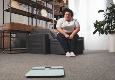 Oturma odasındaki teraziye bakan depresif şişman kadın.