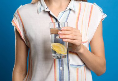 Açık mavi arka planda bir bardak limon suyu olan genç bir kadın., 
