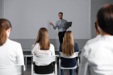 Dizüstü bilgisayarı olan erkek bir işletme eğitmeni konferans odasında projeksiyon ekranlı konferans veriyor.