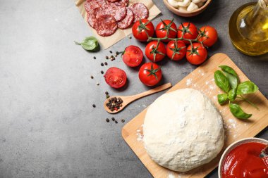 Gri masa üzerinde hamur ve malzemelerle düz kompozisyon, metin için boşluk. Pepperoni pizza tarifi.