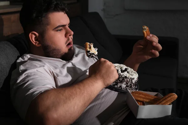 stock image Depressed overweight man eating sweets in living room at night