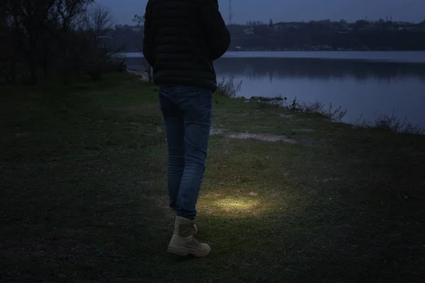懐中電灯を持った男が川の近くを歩いている — ストック写真