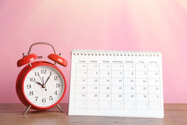 Kalender och väckarklocka på träbord mot rosa bakgrund — Stockfoto