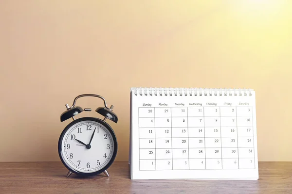 木制桌子上的日历和闹钟对着米黄色的背景音乐 — 图库照片