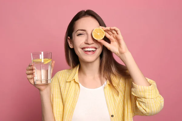 Jonge vrouw met glas citroen water op roze achtergrond — Stockfoto