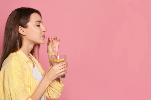 Mladá žena pije citrónovou vodu na růžovém pozadí. Mezera pro t — Stock fotografie