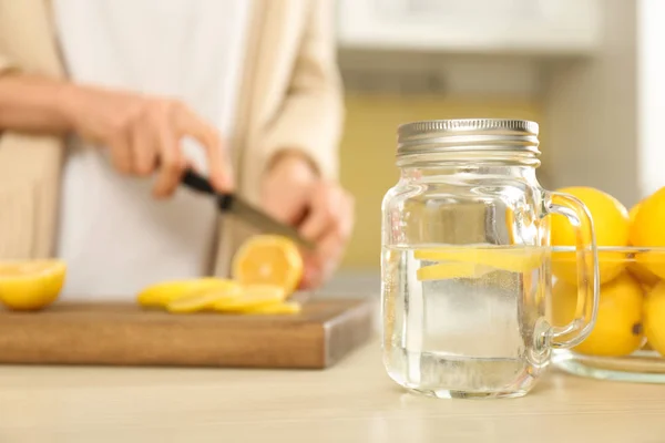 Mujer cortando frutas en la cocina, se centran en tarro de albañil con limón w — Foto de Stock