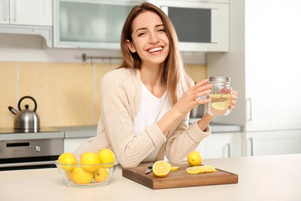 Giovane donna con vaso in muratura di acqua di limone in cucina — Foto Stock