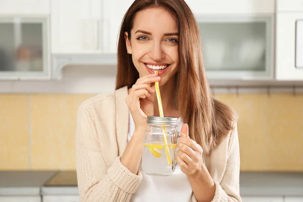 Young woman drinking lemon water in kitchen — Stock Photo, Image