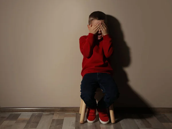 Scared little boy on wooden chair near beige wall, space for tex — Stock Photo, Image