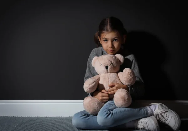 Грустная маленькая девочка с плюшевым мишкой возле черной стены, место для текста . — стоковое фото