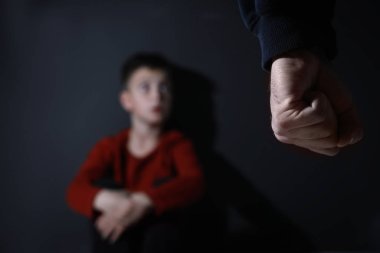 Adam oğlunu siyah arka planda tehdit ediyor, yumruğa odaklanıyor. Aile içi şiddet kavramı