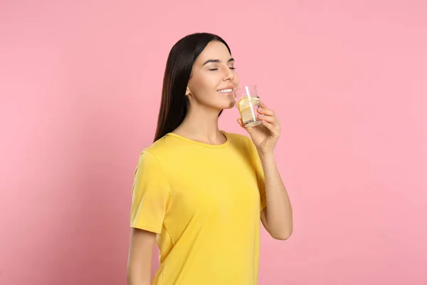 Hermosa joven bebiendo sabrosa agua de limón en rosa backgro — Foto de Stock