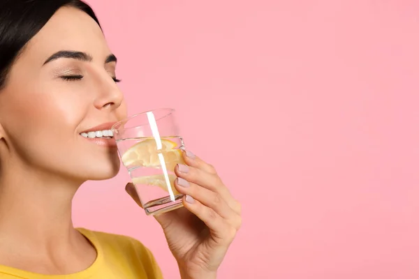 Hermosa joven bebiendo sabrosa agua de limón en rosa backgro — Foto de Stock