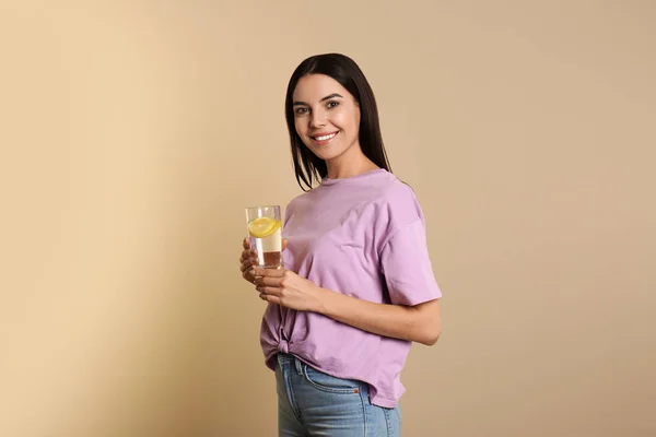 Mulher bonita com água de limão saborosa no fundo bege — Fotografia de Stock