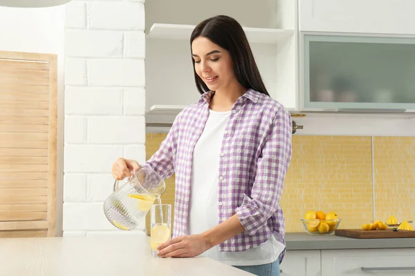 Hermosa mujer joven vertiendo agua de limón en el vaso de la jarra en — Foto de Stock