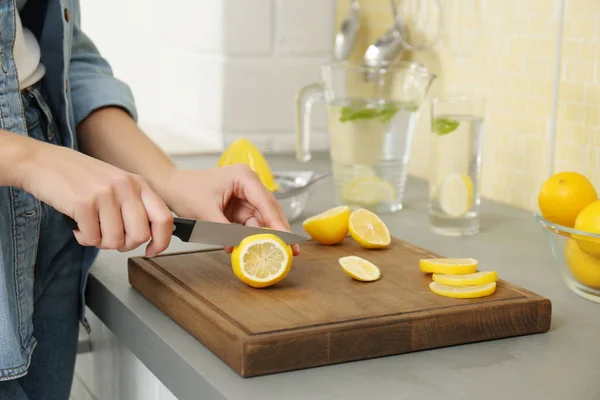 Mujer joven cortando limón para refrescar la bebida en la cocina, cerrar — Foto de Stock