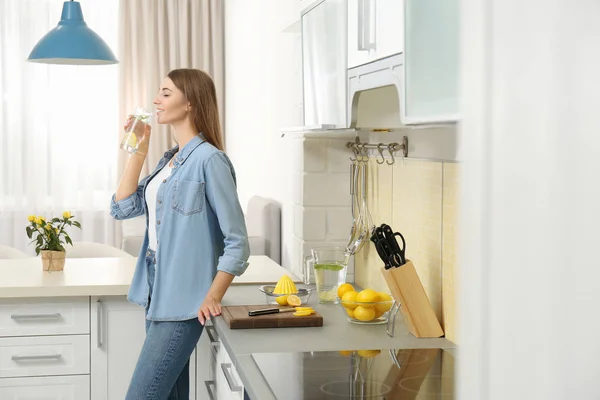 Jovem mulher bebendo água de limão na cozinha — Fotografia de Stock