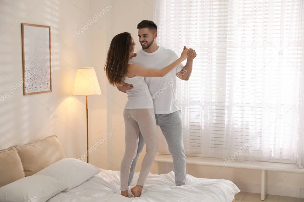 Lovely young couple dancing on bed at home