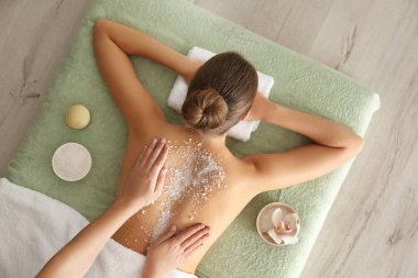 Young woman having body scrubbing procedure with sea salt in spa clipart