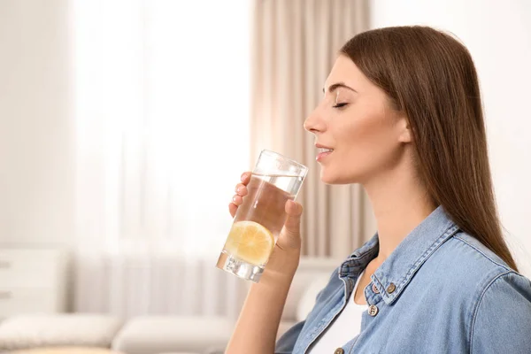 Mujer joven bebiendo agua de limón en casa. Espacio para texto — Foto de Stock